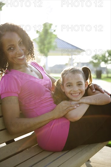 Mother and daughter sitting on park bench