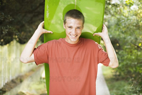 Caucasian teenage boy smiling and holding surfboard