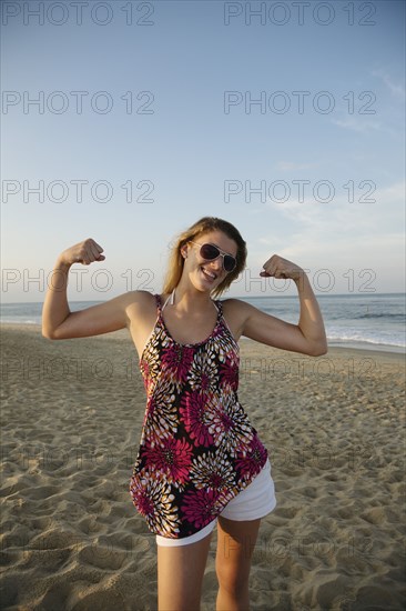 Smiling Caucasian teenage girl flexing biceps on beach