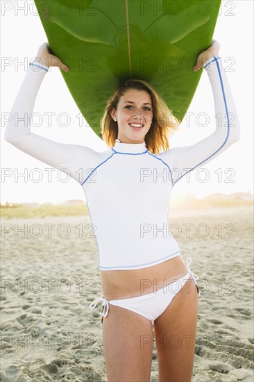 Caucasian teenage girl holding surfboard overhead on beach