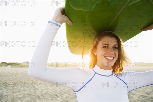 Caucasian teenage girl holding surfboard overhead on beach