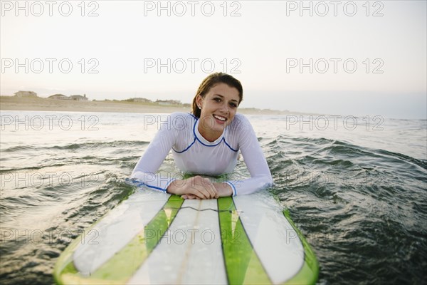 Smiling Caucasian teenage girl leaning on surfboard in ocean