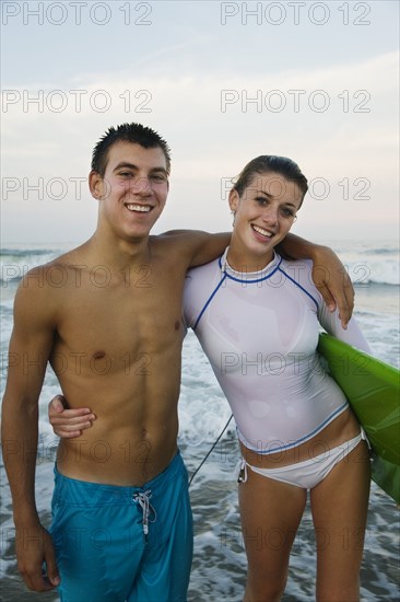 Caucasian teenage couple with surfboard hugging and smiling