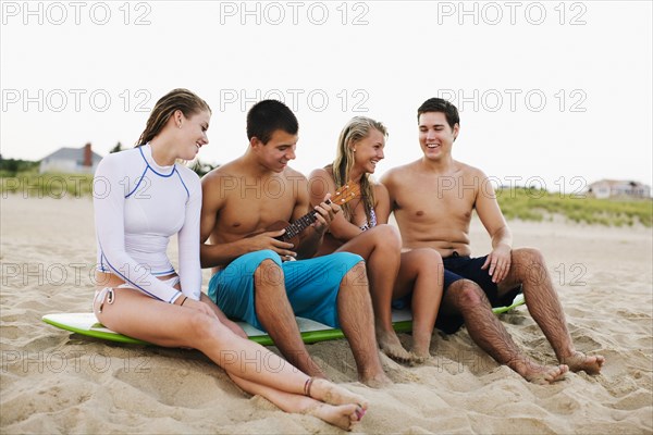 Teenagers sitting on surfboard and playing ukulele on beach
