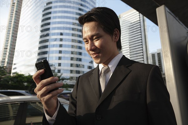 Asian businessman text messaging on cell phone outdoors