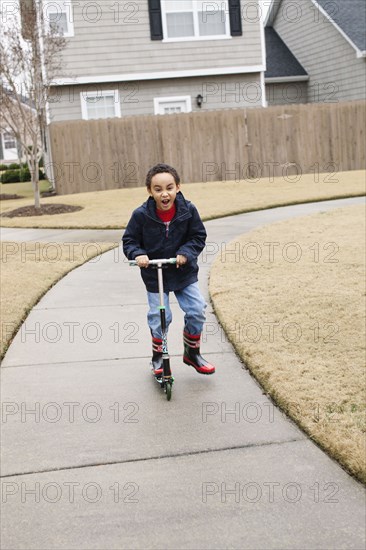 Mixed race boy playing on scooter on suburban street