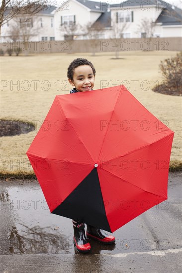 Mixed race boy playing with umbrella in rain