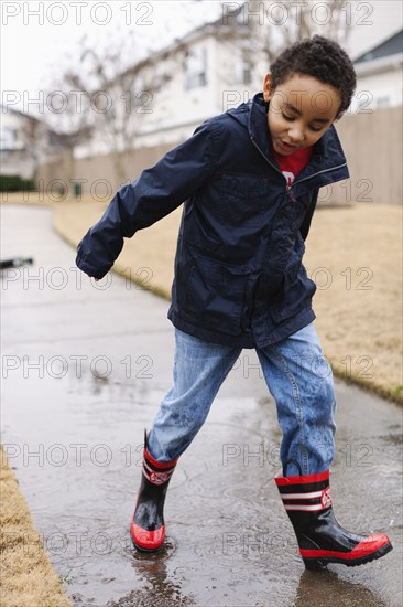 Mixed race boy splashing in rainboots