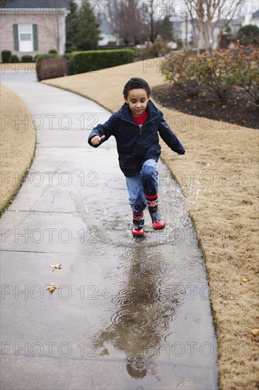 Mixed race boy splashing in rainboots