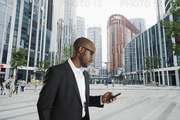 Black businessman using cell phone on city street