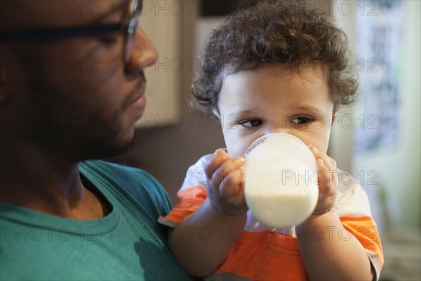 Father helping baby drink bottle in kitchen