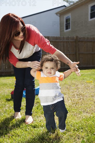 Mother helping baby walk in backyard