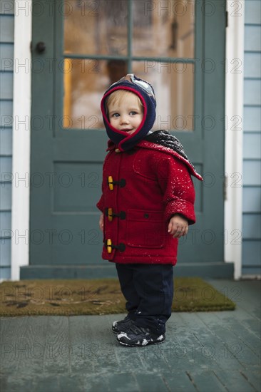 Caucasian boy wearing winter coat on porch