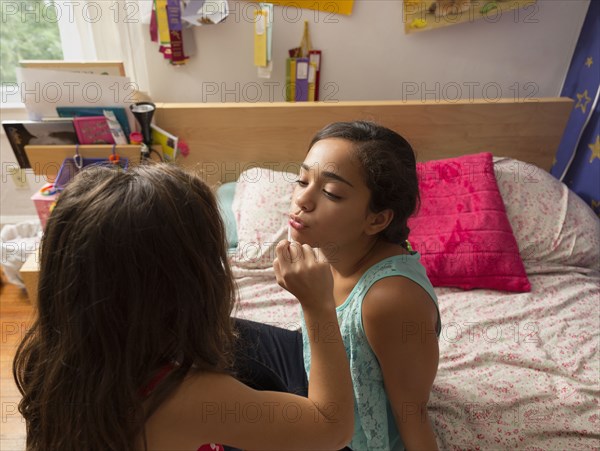 Mixed race girl putting lipstick on sister