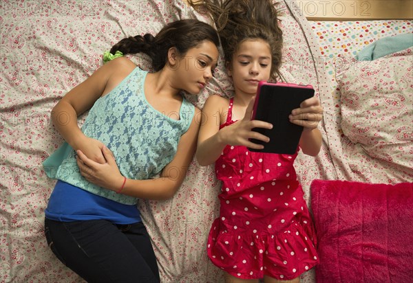 Mixed race sisters using digital tablet on bed