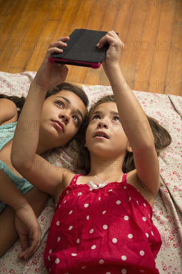 Mixed race sisters using digital tablet on bed