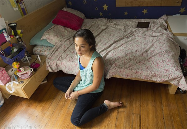 Mixed race girl sitting on bedroom floor