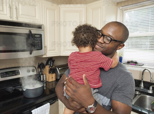 Father holding toddler son in kitchen