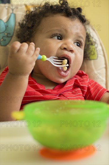 Mixed race toddler boy eating in high chair