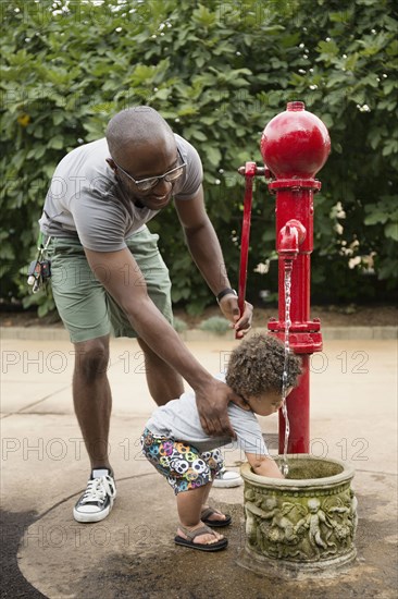 Father and toddler son using water fountain in park