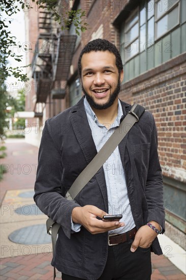 Mixed race businessman using cell phone on city sidewalk