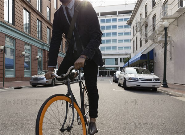 Mixed race businessman riding bicycle on city street