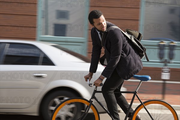 Mixed race businessman riding bicycle on city street