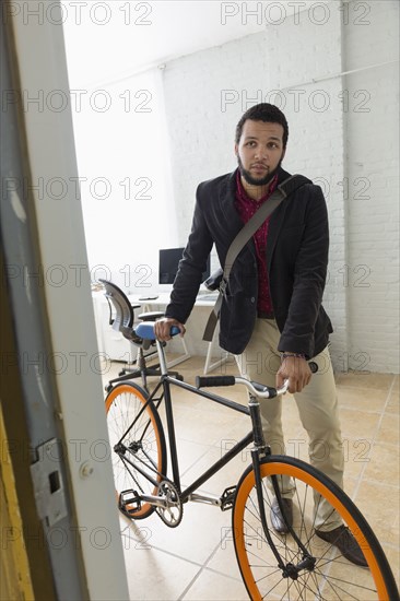 Mixed race businessman wheeling bicycle in office