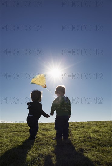 Boys watching kite flying against blue sky