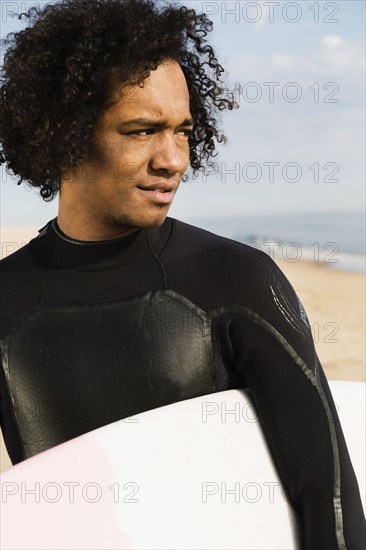 Mixed race surfer carrying board on beach