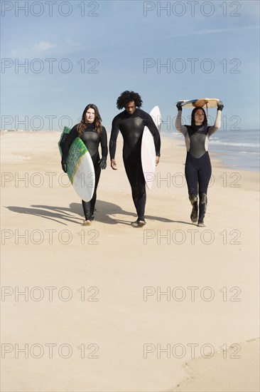 Surfers carrying boards on beach