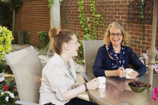 Caucasian mother and daughter drinking coffee in backyard