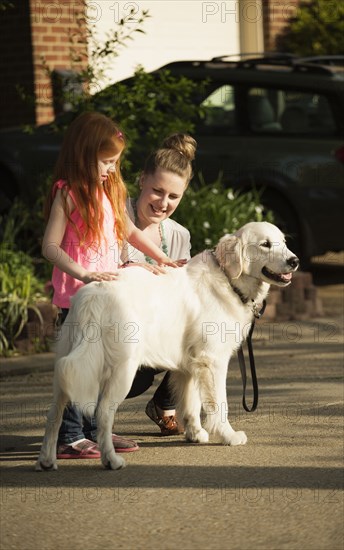 Caucasian mother and daughter petting dog on suburban street