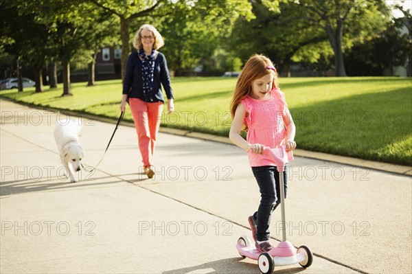 Older Caucasian woman and granddaughter walking dog on suburban street