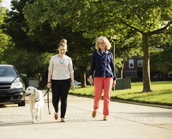 Caucasian mother and daughter walking dog on suburban street