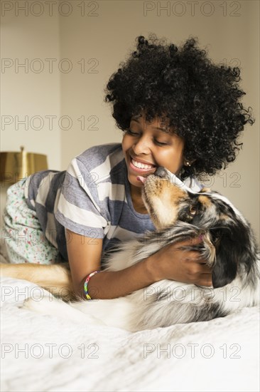 Mixed race woman playing with dog on bed