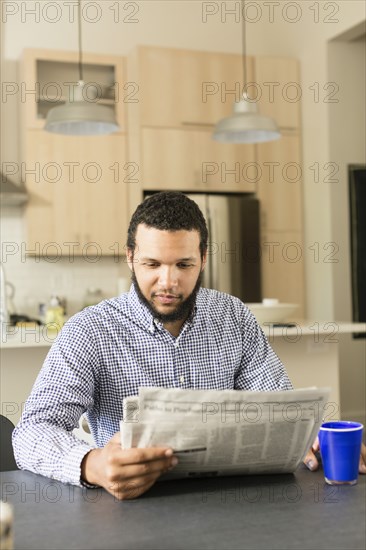 Mixed race man reading newspaper at breakfast table