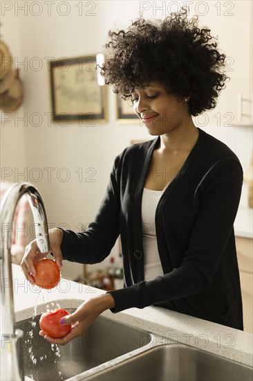 Mixed race woman washing tomatoes in kitchen