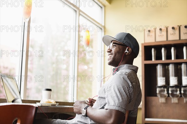 Laughing Black man using laptop in coffee shop