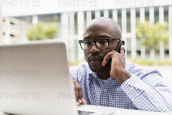 Black man using cell phone and laptop outdoors