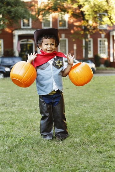 Mixed race boy in cowboy costume holding pumpkin pails on Halloween