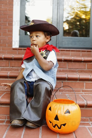 Mixed race boy dressed as cowboy eating Halloween candy