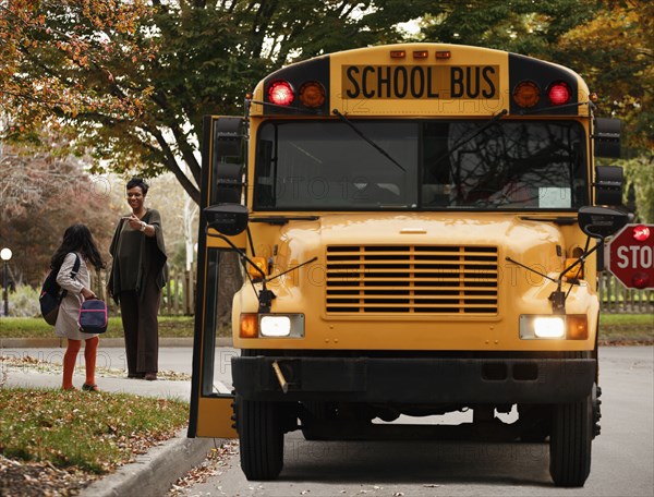 African American woman waiting with daughter for school bus