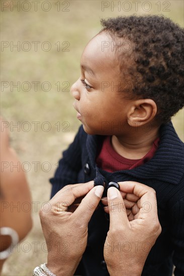 African American mother buttoning sweater of son