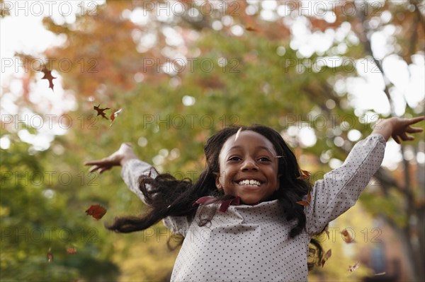 Low angle view of African American girl playing in autumn leaves