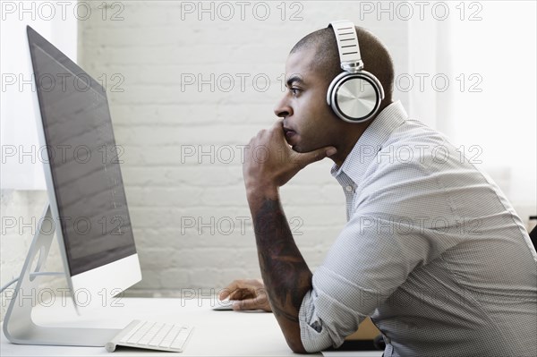 Mixed race businessman listening to headphones and working at desk