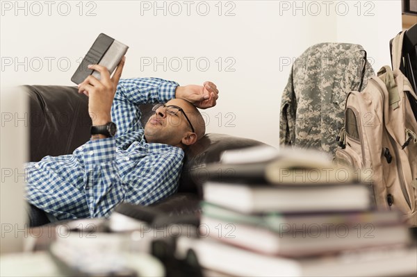 Mixed race man using digital tablet on sofa near books