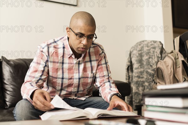 Mixed race soldier reading book on living room sofa