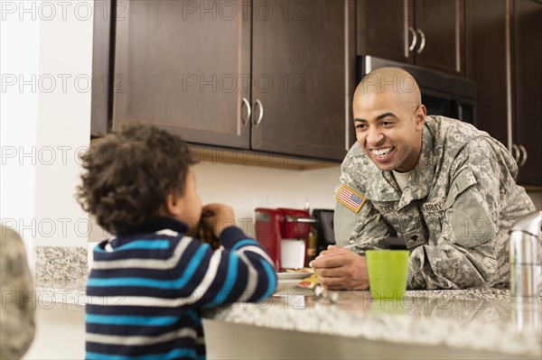 Mixed race soldier father and son eating in kitchen