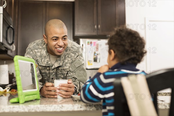 Mixed race soldier father and son eating in kitchen